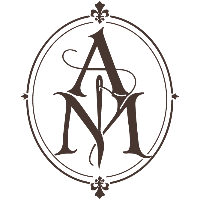 Logo Atelier Mune, une lettre A ce trouve au dessus d'une lettre M, en leur centre une aiguille, le logo est encadré et orné de deux fleurs de lys